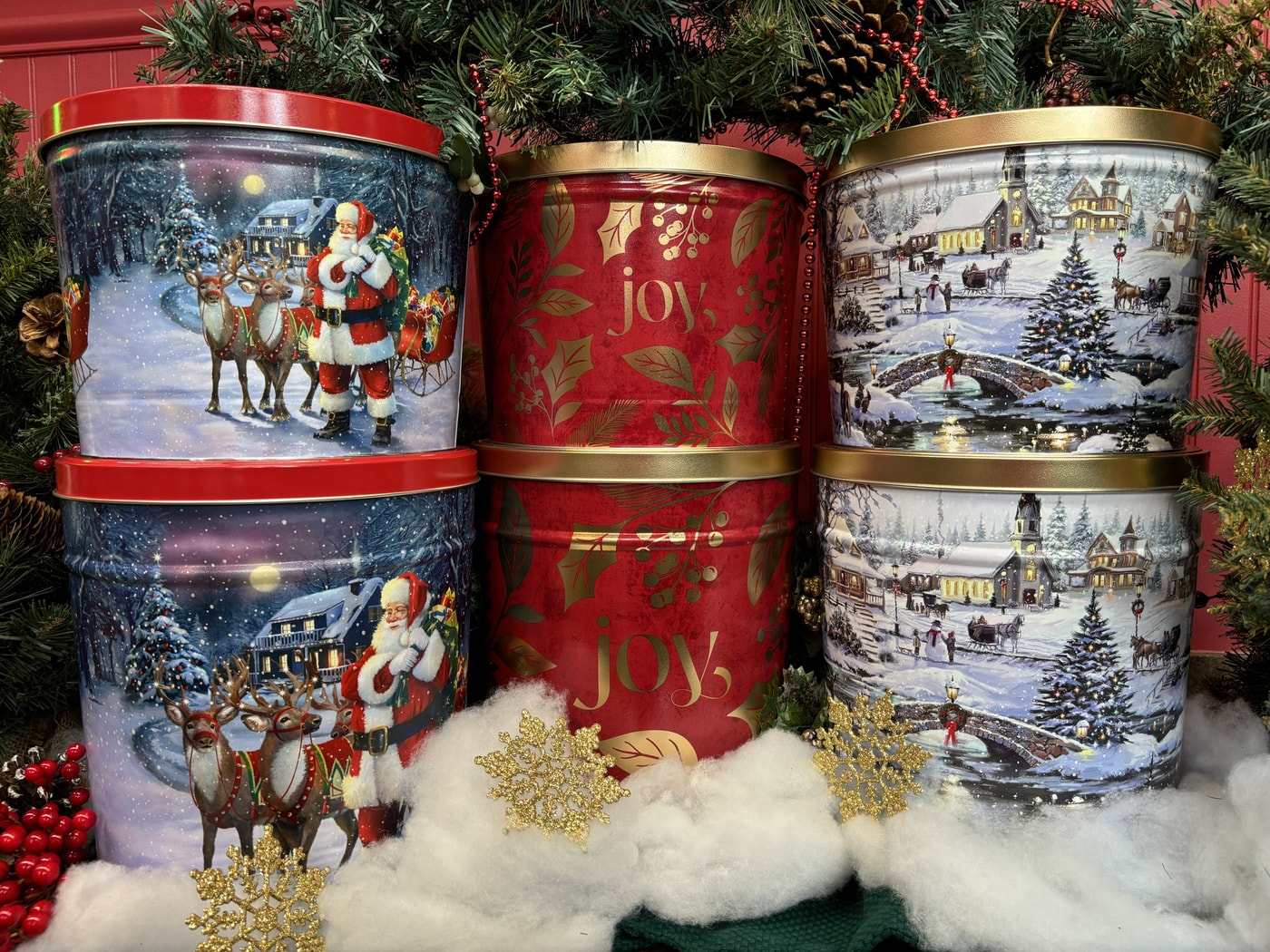 Decorative holiday popcorn tins surrounded by greenery and snow